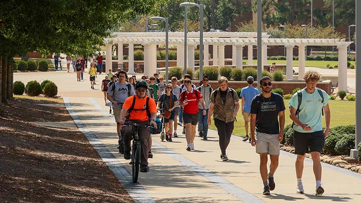 Students walking to class outside on a greenway. ?>