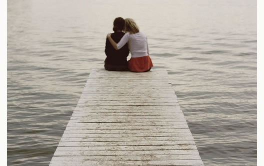 two people sitting at the end of a pier