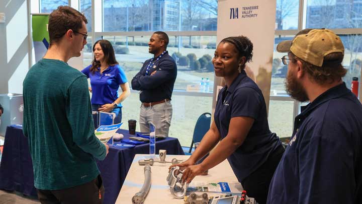 A group of people engage at a career fair, discussing opportunities and examining materials at a Tennessee Valley Authority booth.