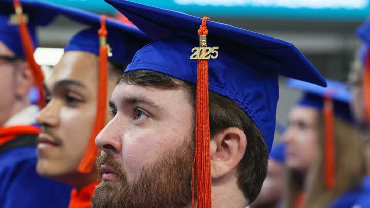 A group of graduates in blue caps and gowns, with a focus on a cap adorned with a '2025' tassel, celebrating their achievement.