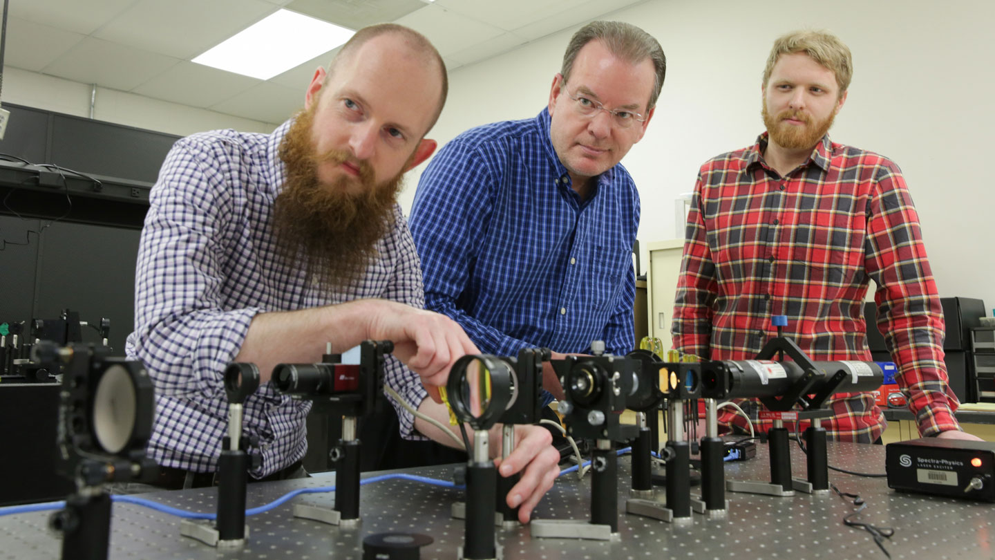 Three men use optical equipment to run an experiment