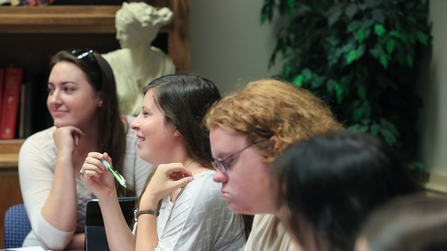 Students listen intently next to a classical sculpture