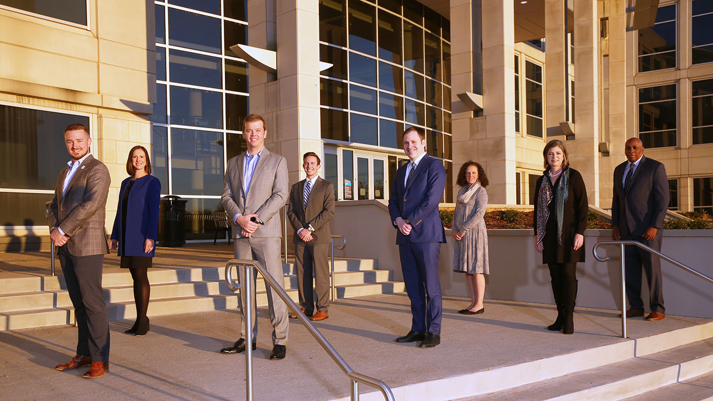 The U A H Alumni Board of Directors standing on the steps of the Shelby Center for Science and Technology building on a sunny late afternoon
