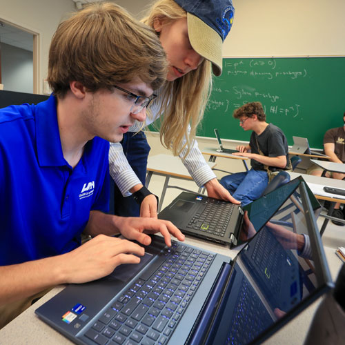 A young man and a woman instructor troubleshoot problems on their laptop computers