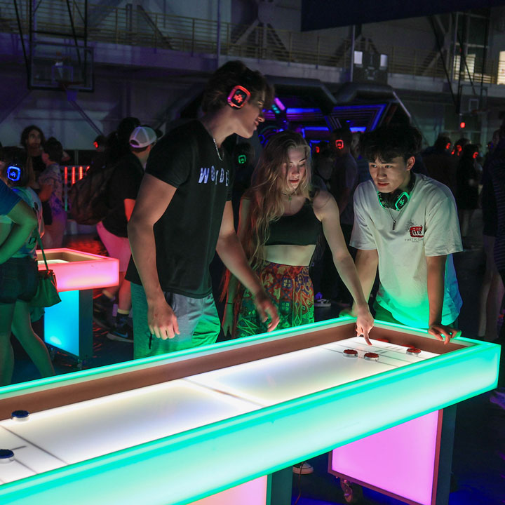 students watch an air hockey game at a glow-in-the-dark party