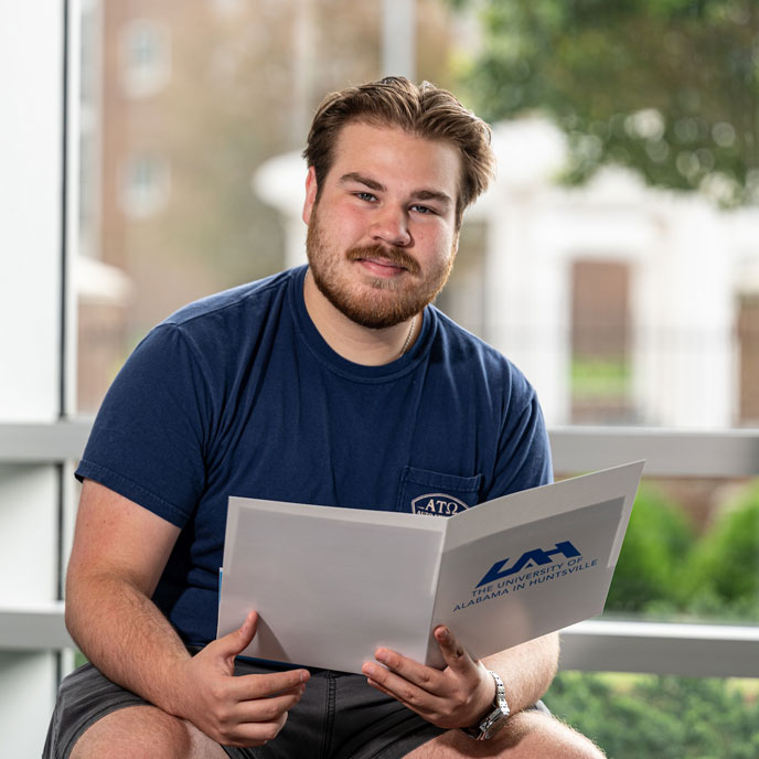 a male student reads U A H admissions resources in the lobby of the student services building.