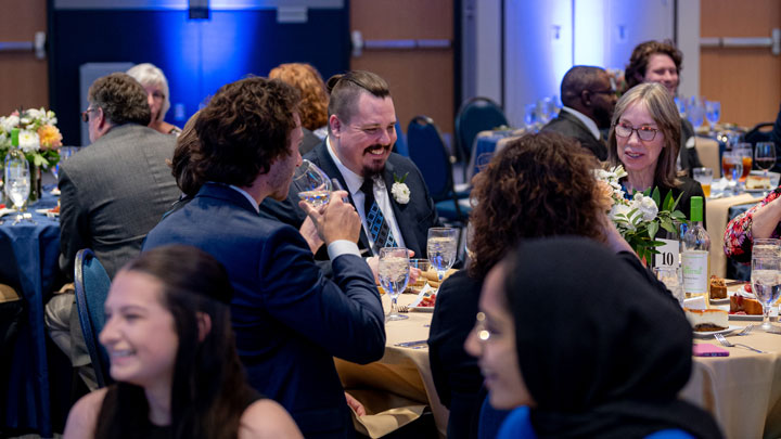 A group of people seated at round tables, engaged in conversation and laughter, at a UAH event.