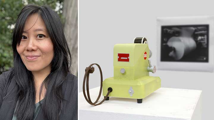 A yellow vintage device with a film reel and a red label, displayed on a pedestal against a neutral background.